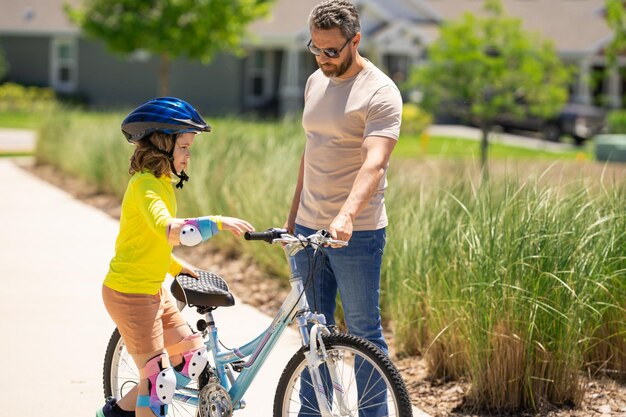 Vater und Sohn mit Fahrradhelm zum Erlernen des Fahrradfahrens im Park. Vater hilft Sohn beim Fahrradfahren