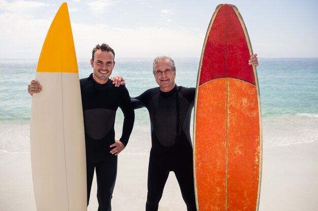 Vater und Sohn mit Surfbrett stehen am Strand