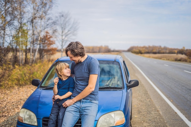 Vater und Sohn ruhen sich auf einem Roadtrip am Straßenrand aus. Autoreise mit Kinderkonzept.