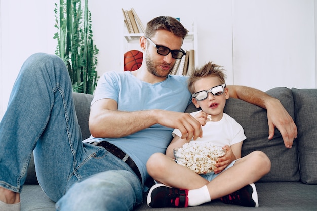 Vater und Sohn schauen Filme zu Hause in 3D-Gläsern und essen Popcorn auf der Couch