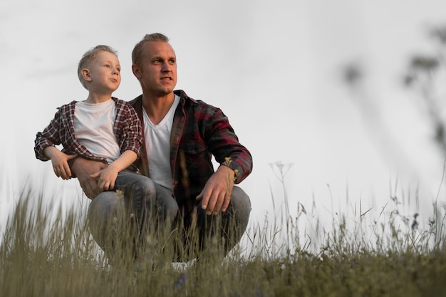 Foto vater und sohn sitzen auf dem feld und beobachten den sonnenuntergang