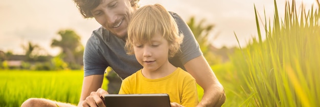 Vater und Sohn sitzen auf dem Feld und halten den Tablet-Jungen, der an einem sonnigen Tag zu Hause auf dem Gras sitzt