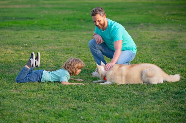 Vater und Sohn sitzen auf dem grünen Gras im Sommerpark oder im Garten Familienurlaub Haustiere lieben Freundschaft