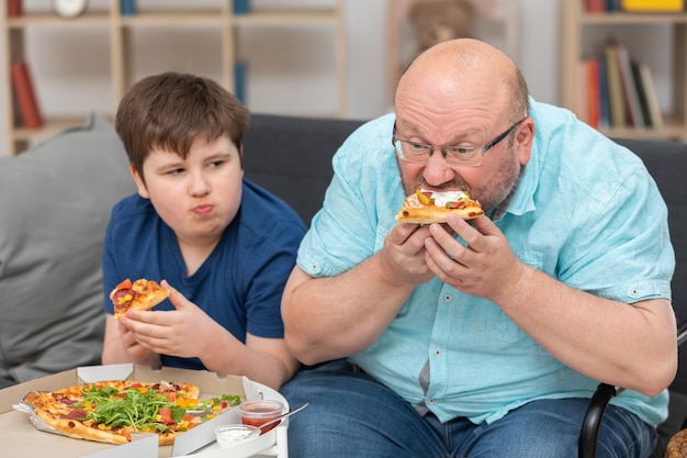 Vater und Sohn sitzen auf dem Sofa im Zimmer und essen Pizza