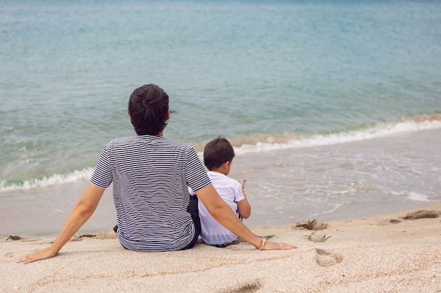 Vater und Sohn sitzen im Sommer im Urlaub am Strand mit Sand