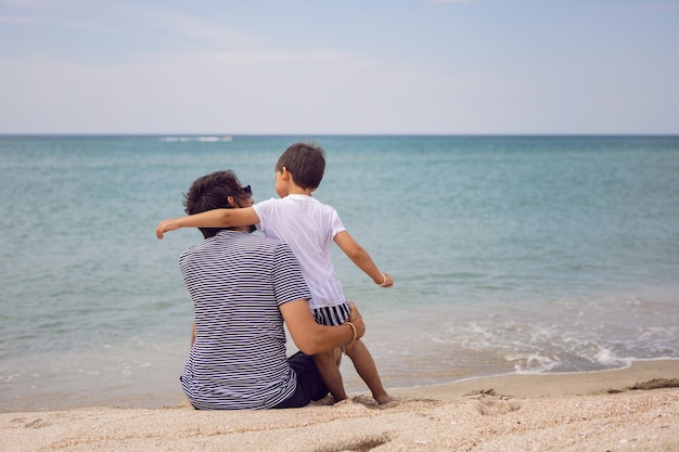 Vater und Sohn sitzen im Sommer im Urlaub am Strand mit Sand