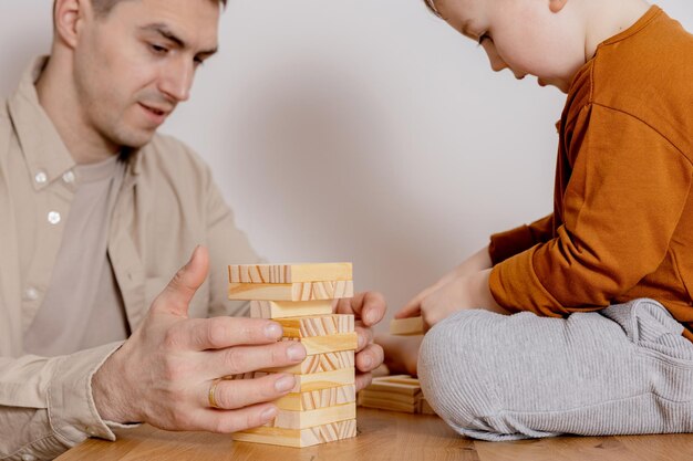 Vater und Sohn sitzen zu Hause zusammen und spielen mit Holzklötzen Jenga-Spiel Kleiner Junge und sein Vater verbringen Zeit miteinander Zeit mit der Familie Freizeitbeschäftigung drinnen