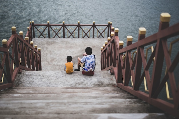 Vater und Sohn sitzen zusammen auf der Brücke in der Nähe des Sees