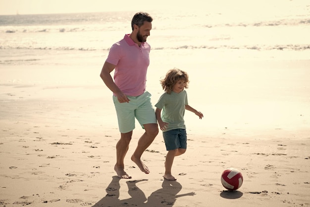 Vater und Sohn spielen Fußball oder Fußball am Strand Papa mit Kind Junge am Sommertag