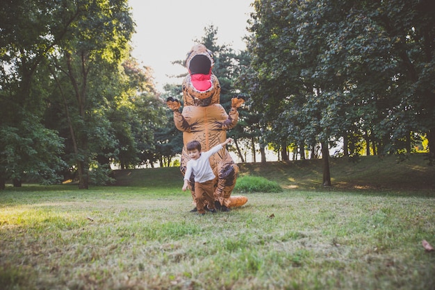 Vater und Sohn spielen im Park mit einem Dinosaurierkostüm und haben Spaß mit der Familie im Freien