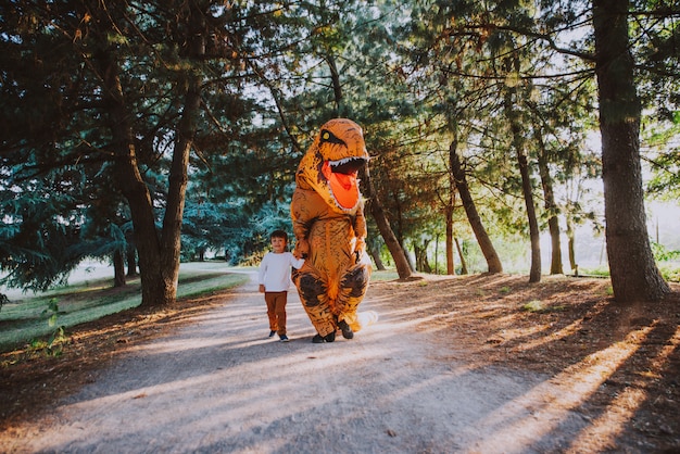 Vater und Sohn spielen im Park mit einem Dinosaurierkostüm und haben Spaß mit der Familie im Freien