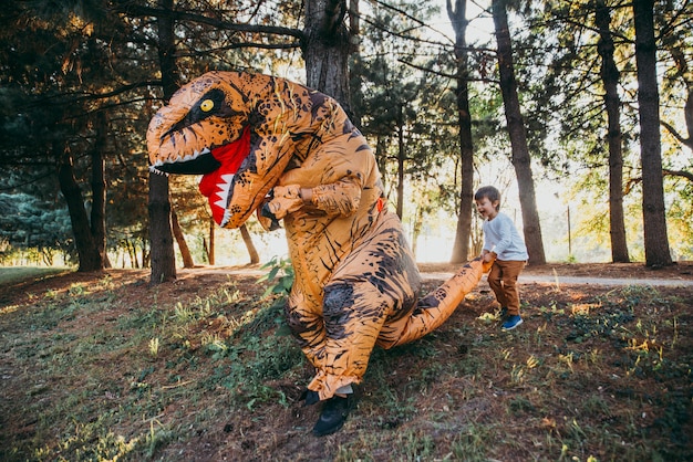 Vater und Sohn spielen im Park mit einem Dinosaurierkostüm und haben Spaß mit der Familie im Freien