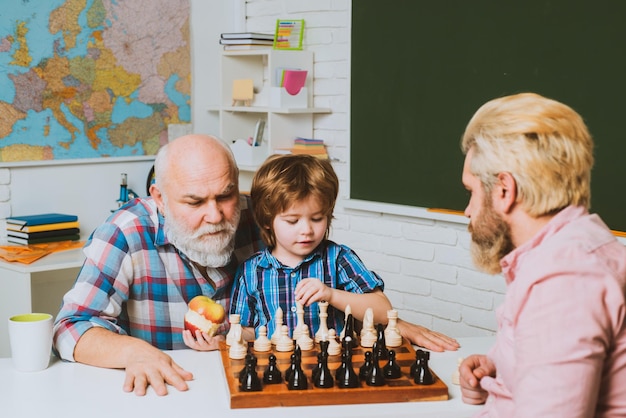 Vater und Sohn spielen in der Schulklasse glücklich lächelnder Enkeljunge mit Vater und Großvater, die Schach spielen