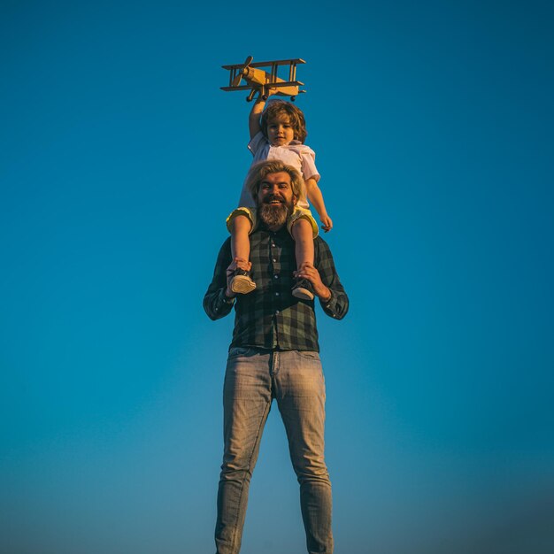 Vater und Sohn spielen mit Holzflugzeug. Junge sitzt auf den Schultern des Vaters.