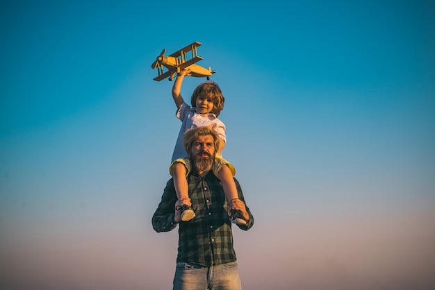 Vater und Sohn spielen mit Holzflugzeug. Vater trägt seinen Sohn auf den Schultern.