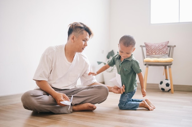 Vater und Sohn spielen mit Papierflieger und lächeln, während sie zu Hause Zeit miteinander verbringen