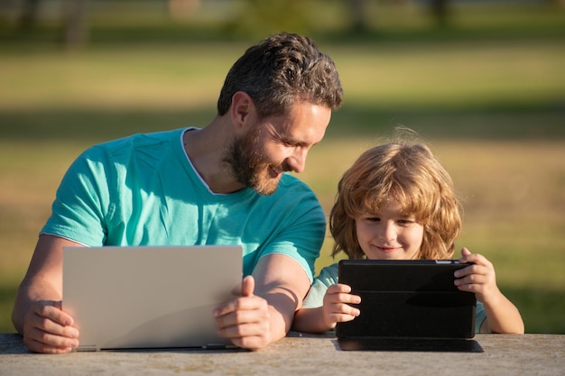 Vater und Sohn spielen oder lernen mit Laptop im Park