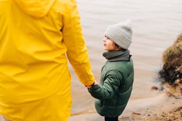Vater und Sohn stehen am Ufer des Sees und halten sich an den Händen glückliche Familie mit spielendem Kinderjunge