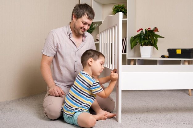 Vater und Sohn stellen ein Kinderbett aus Holz zusammen