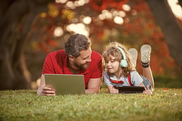 Vater und Sohn verwenden Laptop für Videoanrufe oder Unterrichtsstunden, hören Musik über Kopfhörer in der Parkerziehung online