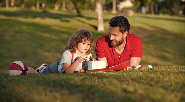 Vater und Sohn zeichnen glücklichen Vatertag im Freien glückliche Familie Vater und Kind Junge entspannen sich auf Gras im Park Kind halten Lernen, Kindheit und Vaterschaft zu zeichnen, verbringen Zeit miteinander