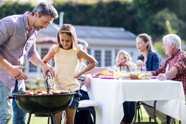 Vater und Tochter am Grill grillen während die Familie, die zu Mittag isst