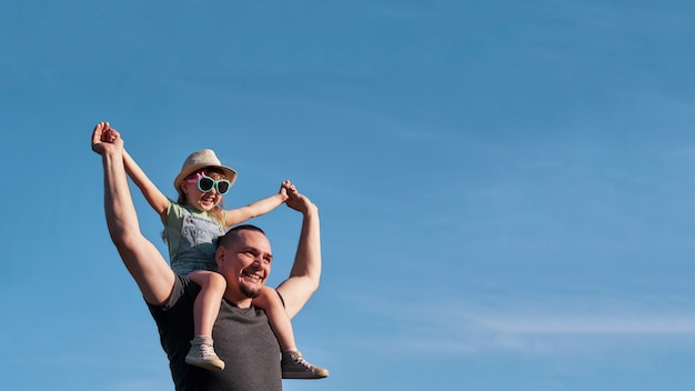 Vater und Tochter auf den Schultern freuen sich glücklich. Vater hält kleine Tochter, die auf dem Flug sitzt, ahmt den Vater nach.