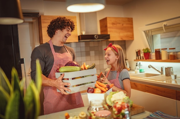 Vater und Tochter bringen Kisten voller Gemüse in die Küche und bereiten sich auf das Kochen vor.