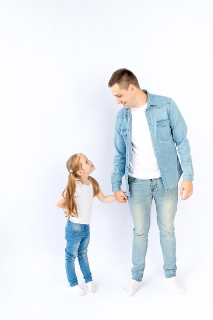 Vater und Tochter halten Händchen und schauen sich in einem blauen Jeanshemd auf einem weißen isolierten leeren Hintergrund in einem Fotostudio an glückliche Familie oder Vaterschaft leerer Platz für Text