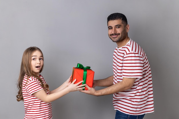 Vater und Tochter in gestreiftem, feierndem Kindergeburtstagsvater, der dem erstaunten Kind eine Geschenkbox gibt