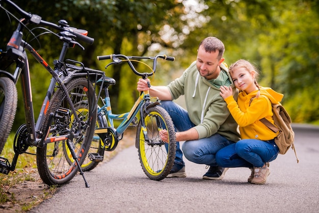 Vater und Tochter inspizieren das Rad des Kinderfahrrads im Teenageralter auf dem Herbstweg des Parks