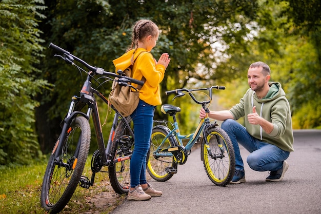 Vater und Tochter inspizieren das Rad des Kinderfahrrads im Teenageralter auf dem Herbstweg des Parks