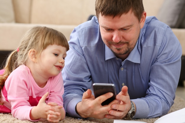 Vater und Tochter liegen am Boden mit Handy