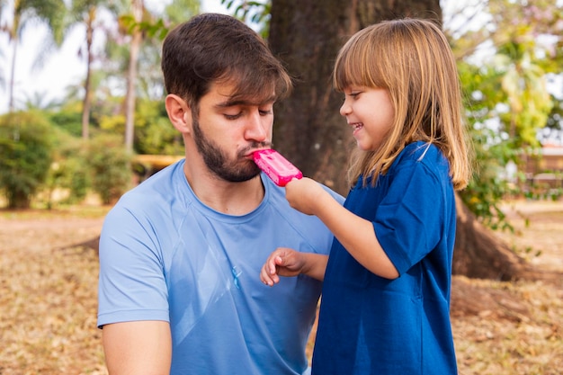 Vater und Tochter lutschen im Park an einem leckeren Eis am Stiel