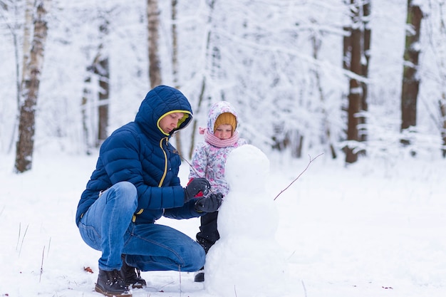 Foto vater und tochter machen im winterwald einen schneemann