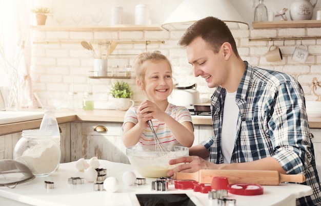 Vater und Tochter machen Kekse und mischen Teig in einer Schüssel. Familienwochenende, kulinarisches und backendes Konzept, Kopienraum
