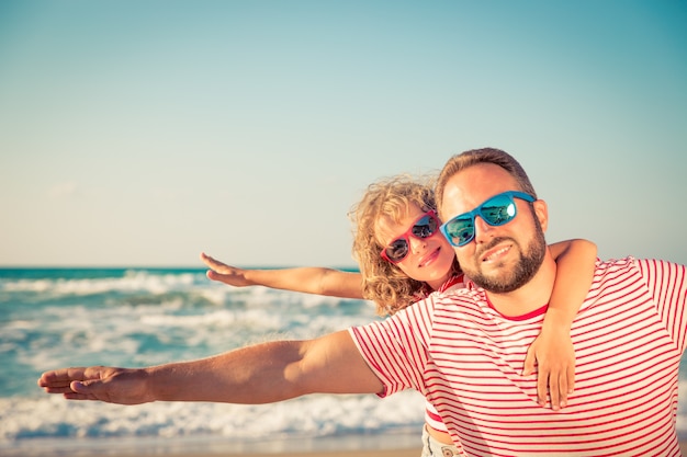 Vater und Tochter mit einem Arm ausgestreckt und umarmt vor blauem Meer- und Himmelshintergrund