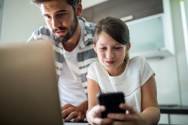 Vater und Tochter mit Laptop und Handy im Wohnzimmer