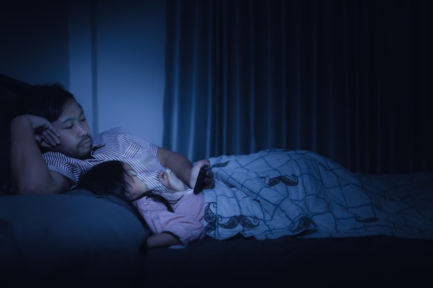 Vater und Tochter schlafen im Schlafzimmer auf dem Bett. Zeichentrickfilm mit Telefon ansehen. Vatertag-Konzept