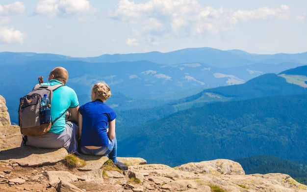 Vater und Tochter sitzen auf einem Felsen auf blauen Bergen