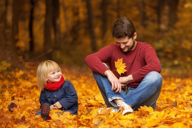 Vater und Tochter sitzen und lachen in einem Herbstpark. Spielen und Spaß haben