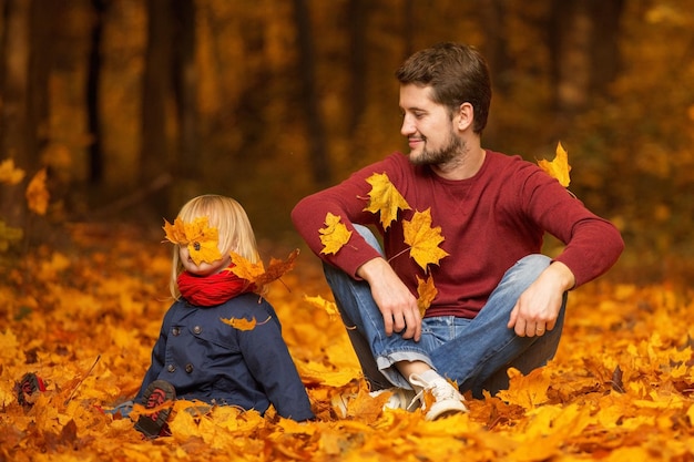 Vater und Tochter sitzen und lachen in einem Herbstpark. Spielen und Spaß haben