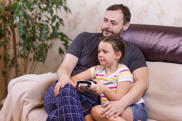 Vater und Tochter sitzen zu Hause auf dem Sofa und spielen Videospiel