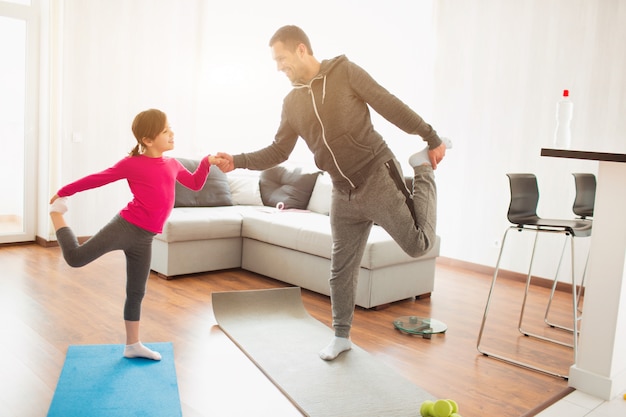 Vater und Tochter trainieren zu Hause. Training in der Wohnung. Sport zu Hause. Sie machen Übungen mit Yoga oder Pilates.