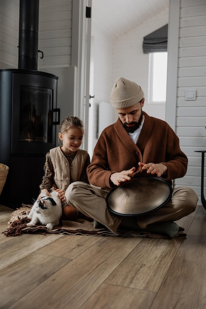 Vater und Tochter verbringen Zeit zusammen, sitzen nebeneinander und spielen Handpan, teilen die Zeit zu Hause, spielen mit einer Katze und wärmen sich am heißen Kamin.