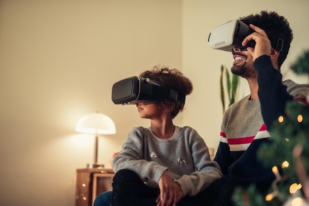 Vater und Tochter verwenden VR-Headset, während sie neben dem Weihnachtsbaum sitzen