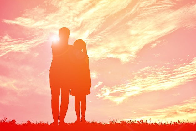 Vater und Tochter vor einem bewölkten Himmel beim Sonnenuntergang