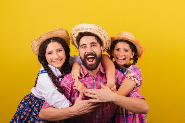 Vater und Töchter, die typische Kleidung für die Festa Junina tragen, umarmen sich glücklich und lächelnd für die Arraia-Party