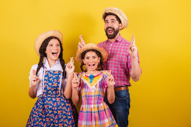 Vater und Töchter tragen typische Kleidung für die Festa Junina mit gekreuzten Fingern und wünschen hoffnungsvoll Für die Arraia-Party