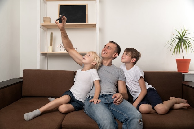 Vater und zwei Söhne machen ein Selfie, während sie auf der Couch sitzen. Freizeit mit Kindern.